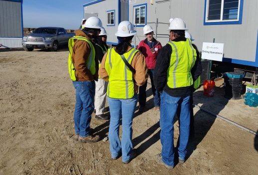 Koloma field team in safety vests and hard hats discussing drilling operations on site